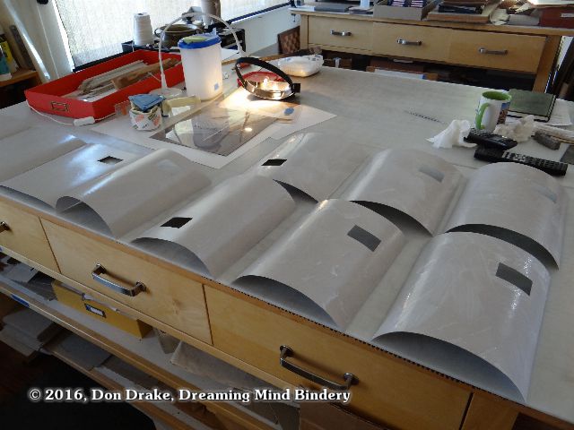 Chipboard layers of laminated book covers right after the application of priming adhesive showing the influence of moisture on the material.