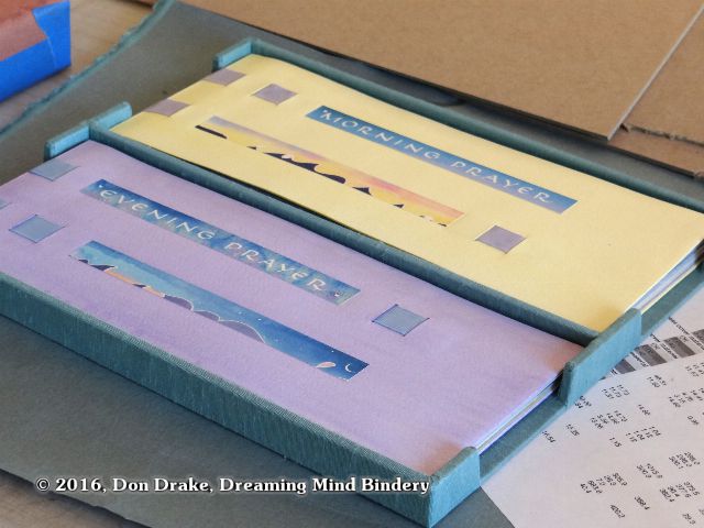 A box containing two paper bound books with arched lift-panels underneath them